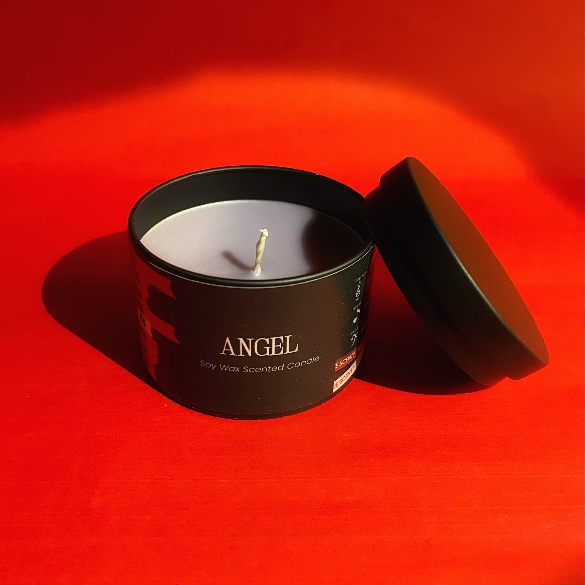 Candle in a black container labeled 'Angel' on a red background. BTS 
