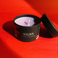 Scented candle in a black container labeled 'GOLDEN' on a red background- bts JK, jungkook 